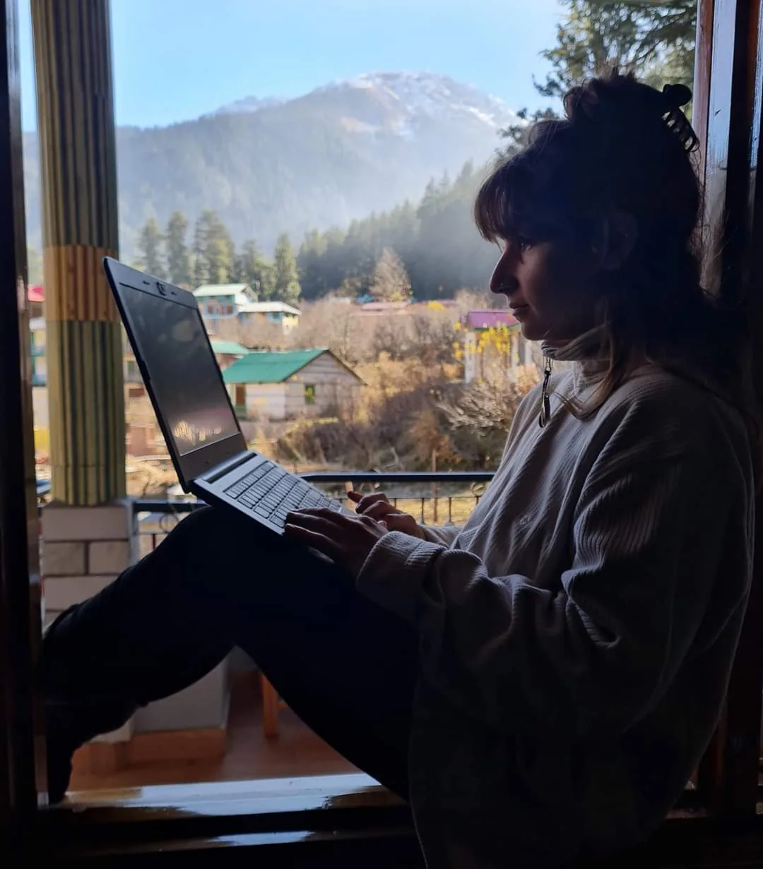 Noam working on a laptop by a window, mountains outside